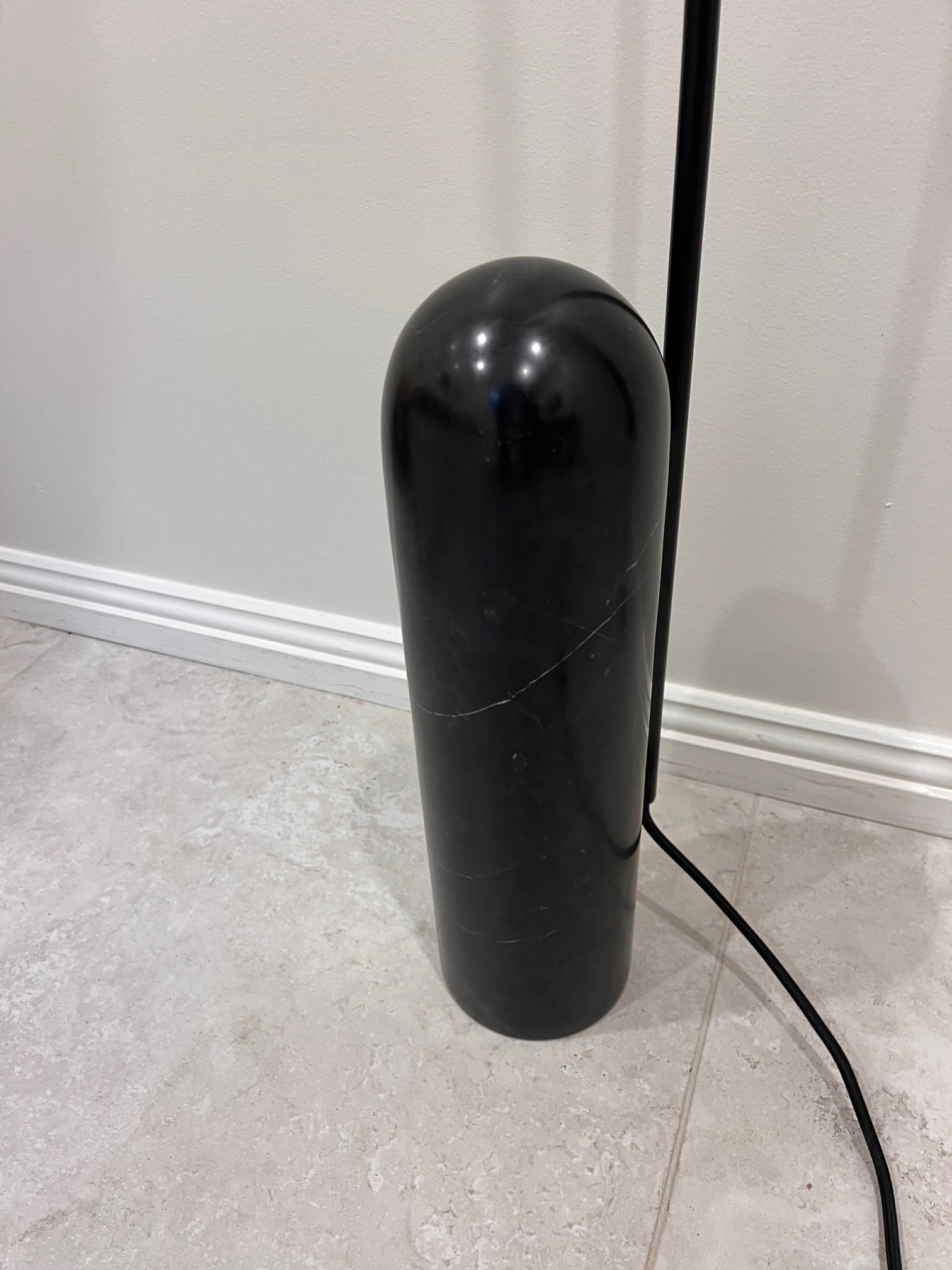 Black cylindrical object on a tiled floor with a white wall background