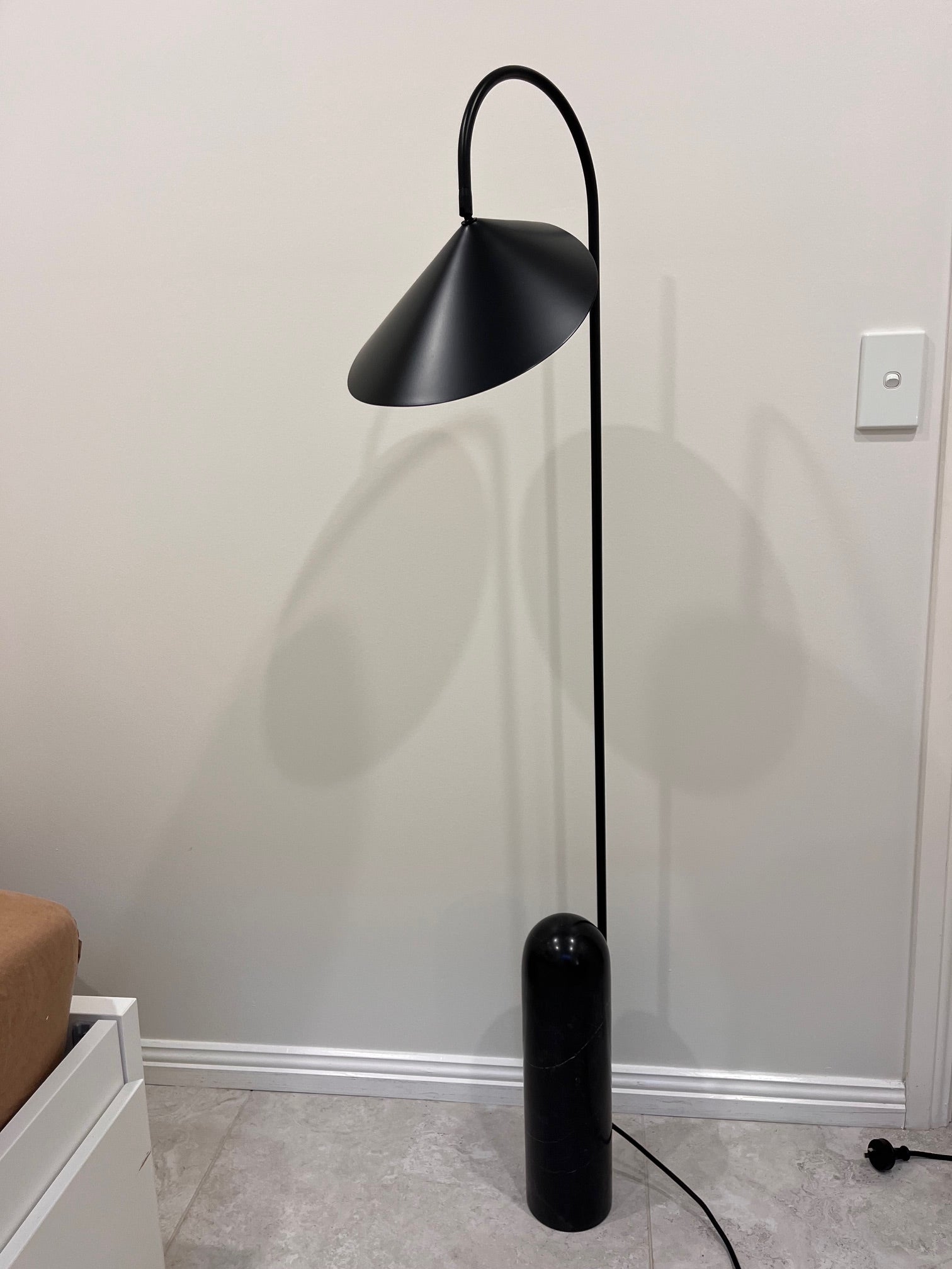 Black floor lamp against a white wall with a light switch visible.
