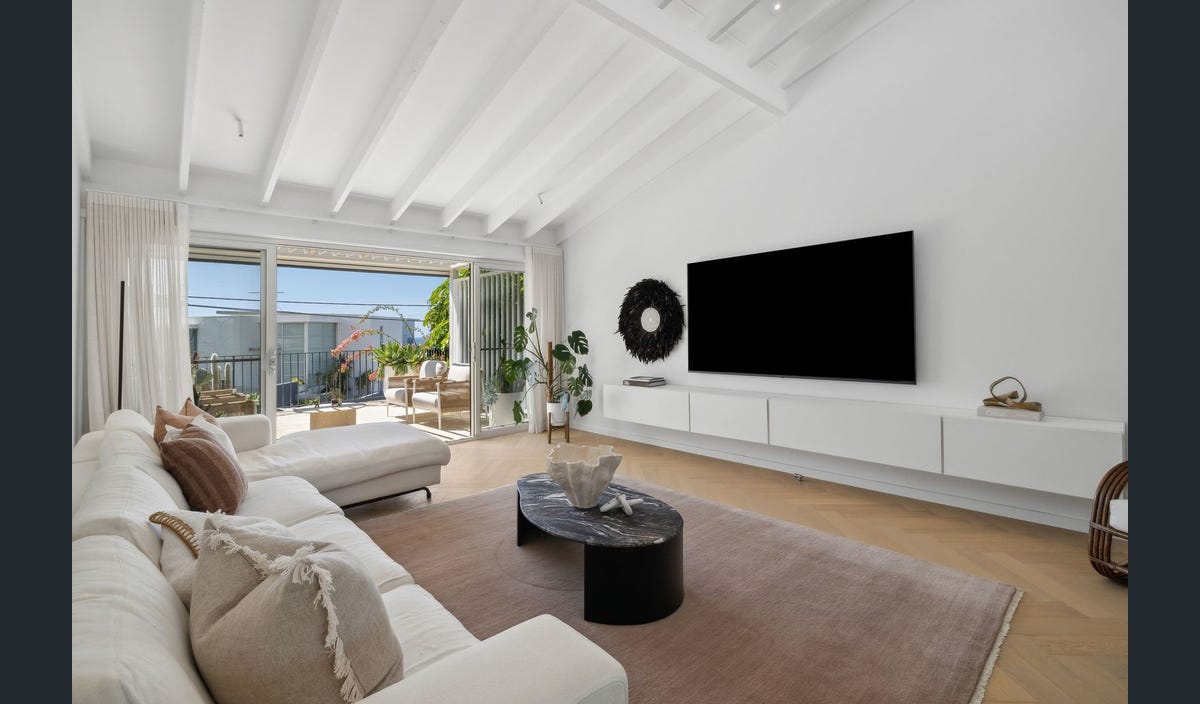 Modern living room with white walls, wooden floor, and a large TV.
