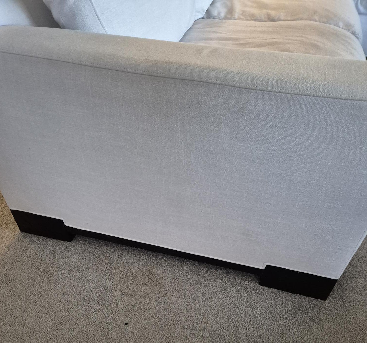 Gray upholstered ottoman with black legs on a carpeted floor.
