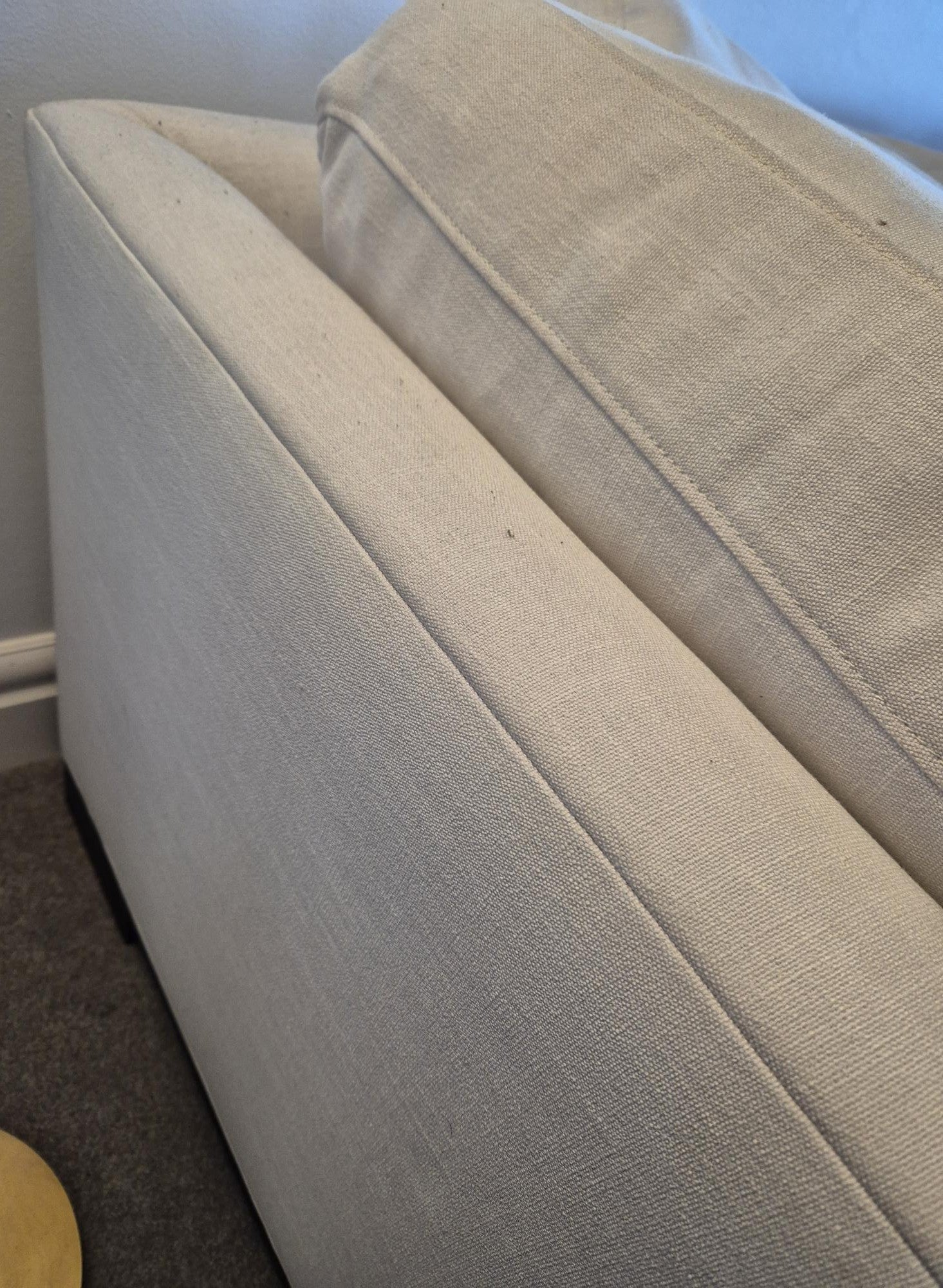 Beige sofa with a stain on the cushion in a room setting.