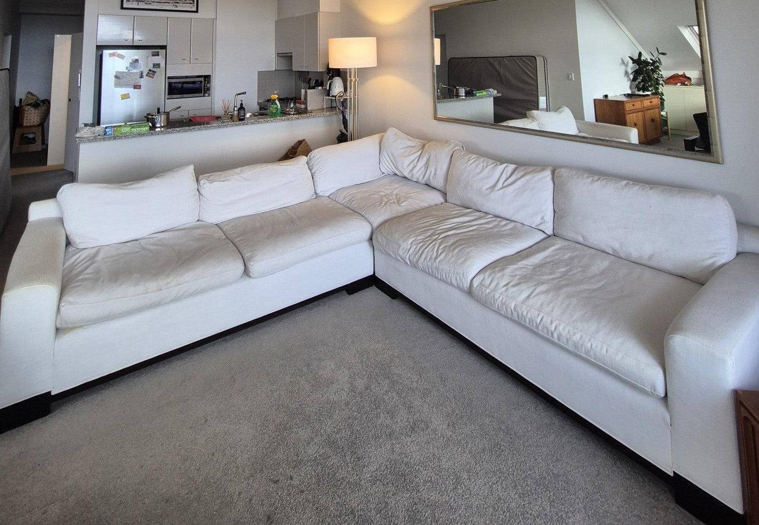 White sectional sofa in a living room with a kitchen in the background