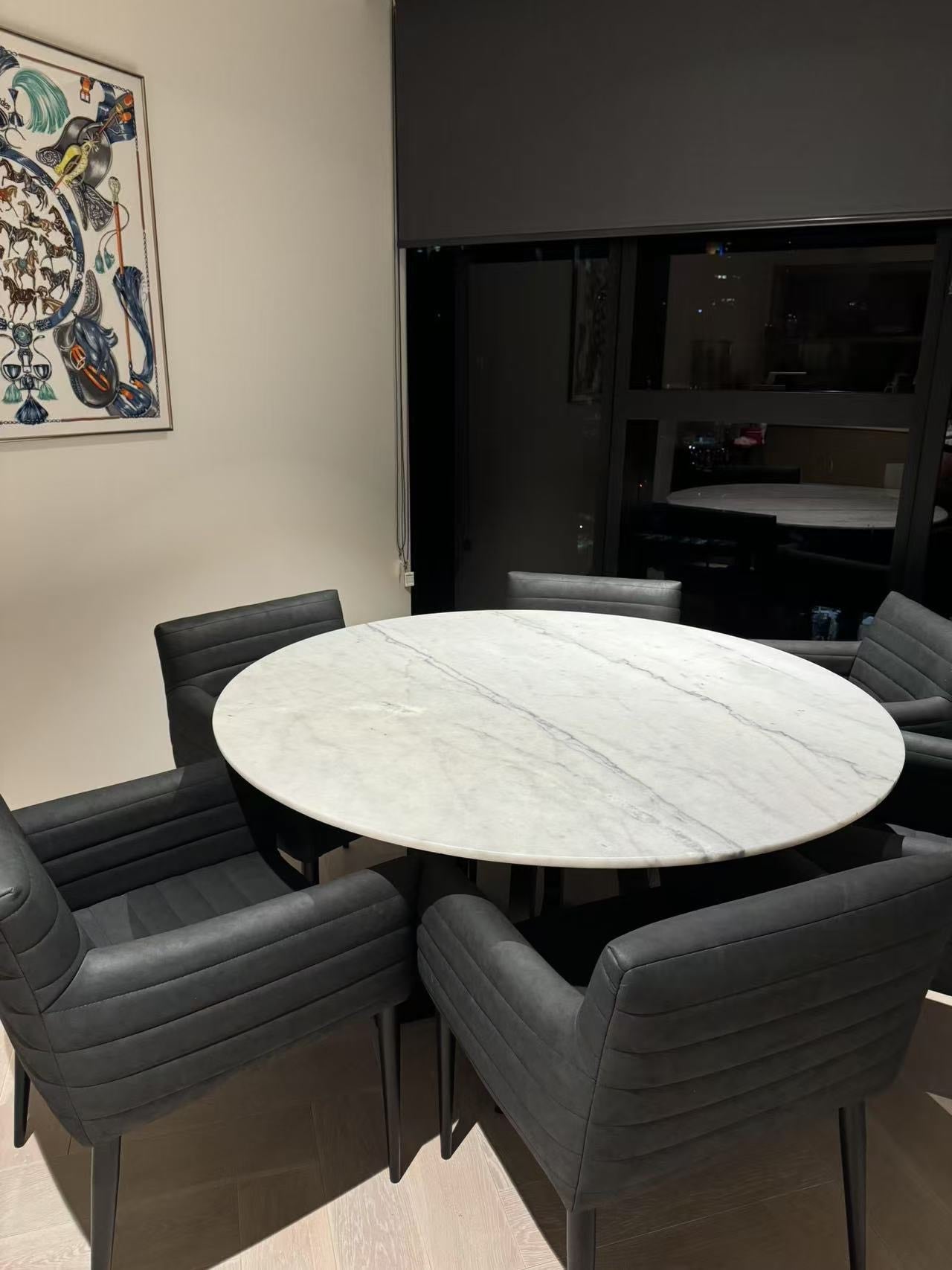Dining area with a round marble table and black chairs in a modern room.
