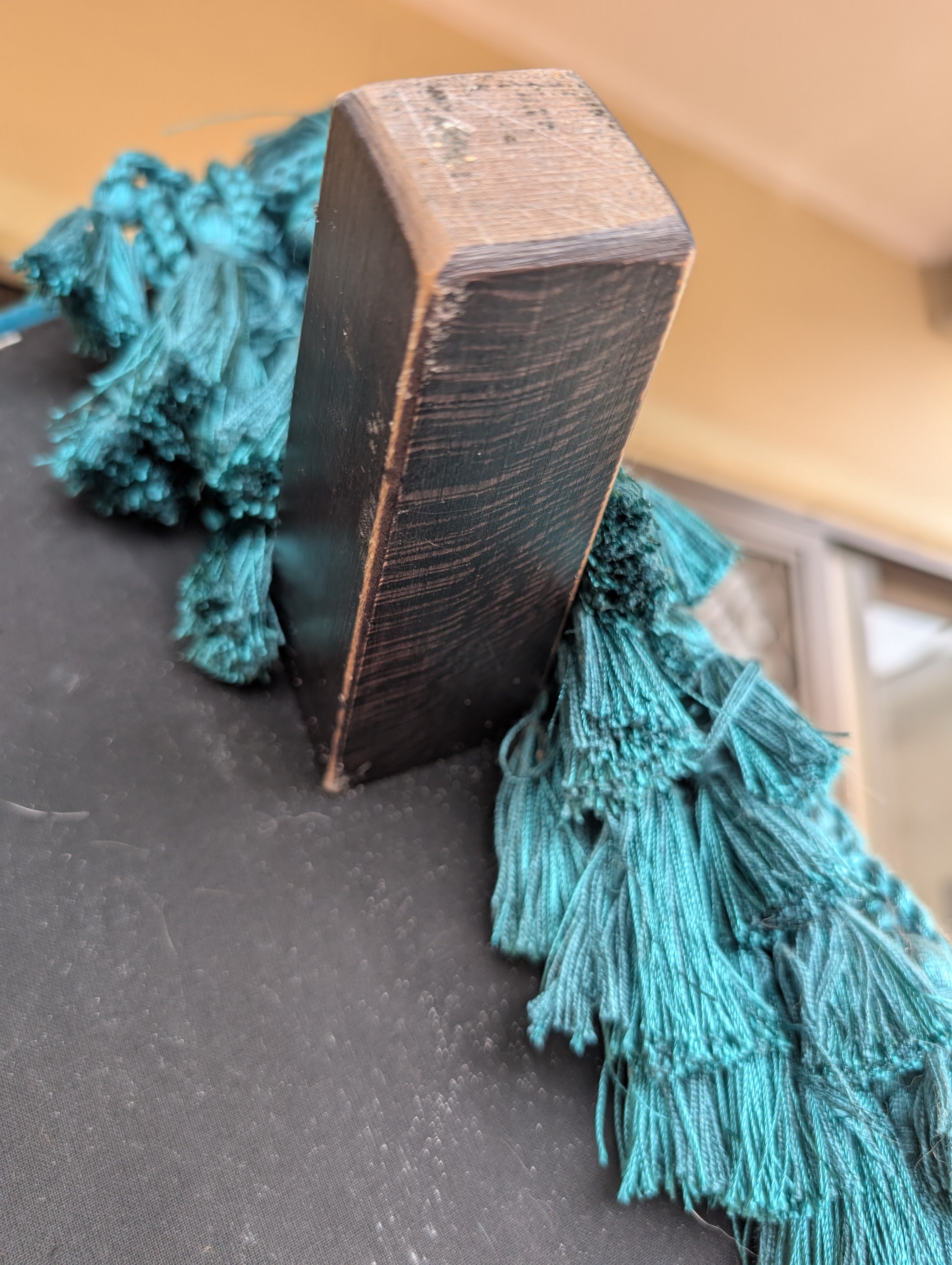 Teal tassels attached to a wooden block on a gray surface.