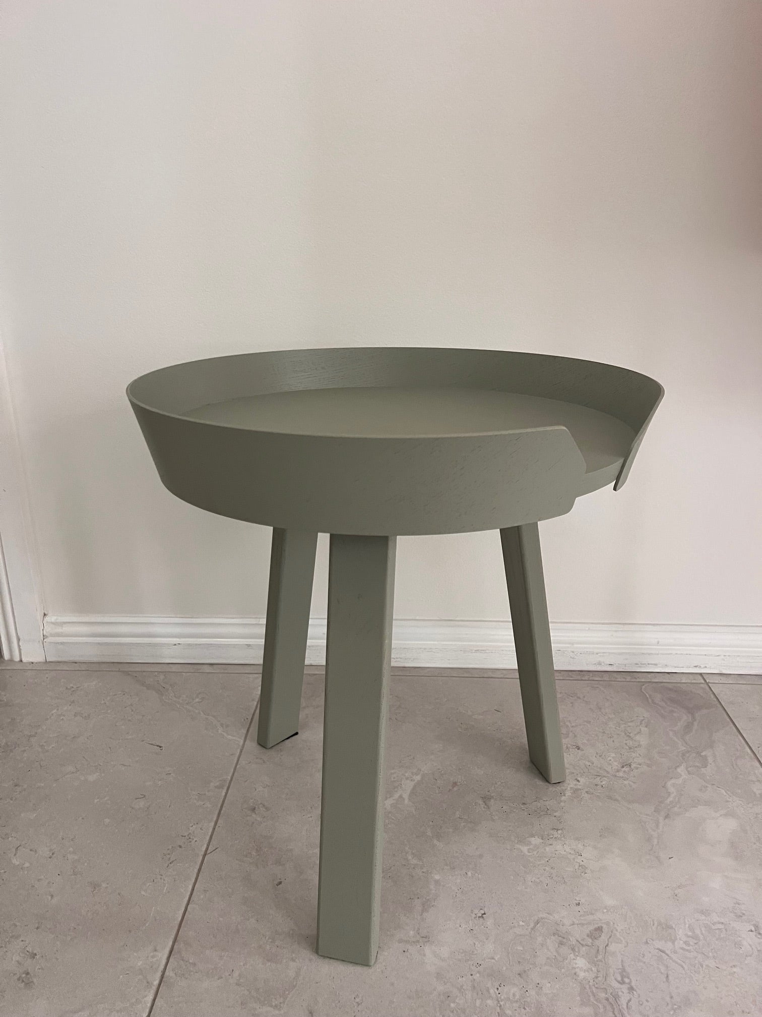 Green side table with a round top and four legs on a light gray floor.