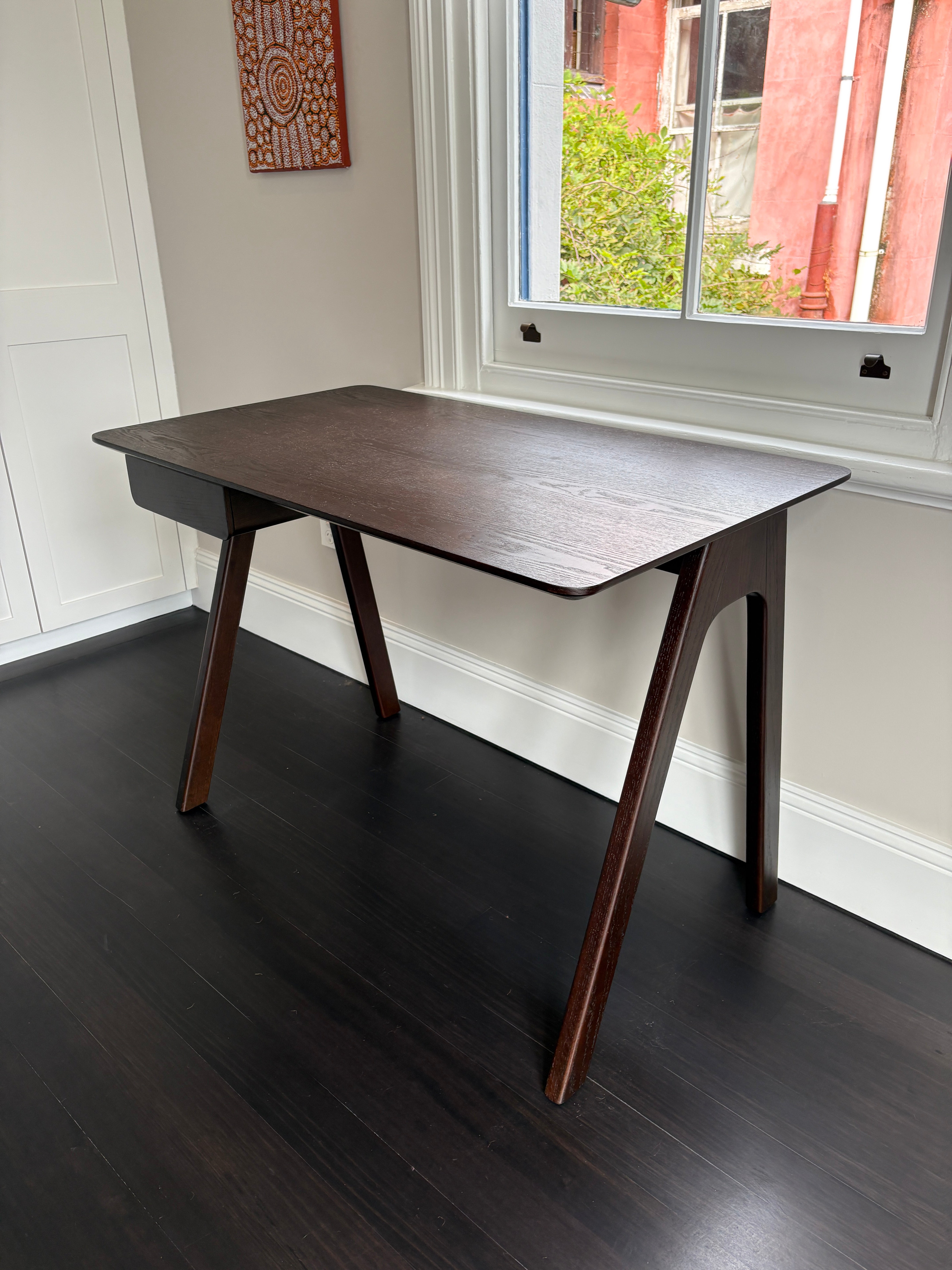 Wooden desk in a room with a window and decorative wall art.