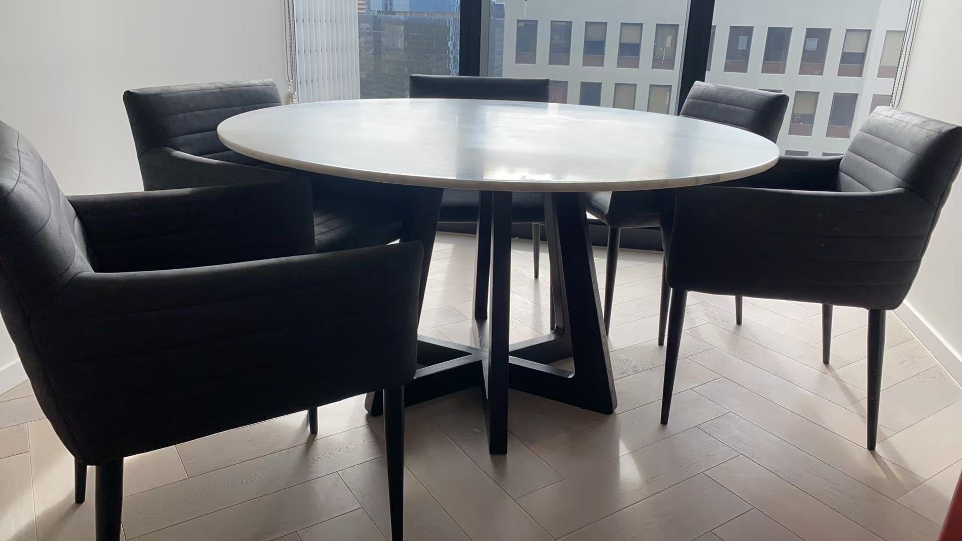 Round dining table with six black chairs in a modern room.