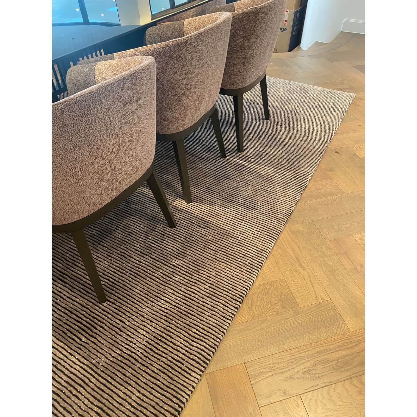 Three brown chairs on a striped rug next to a wooden floor.